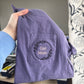 Purple shirt with 'Girl Mom' embroidery held by a person in an office setting.